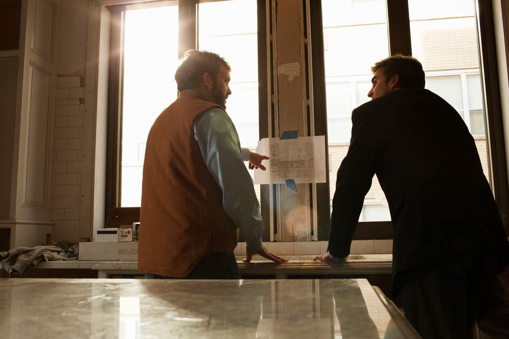 Två personer som står på en byggarbetsplats framför en planritning och planerar.